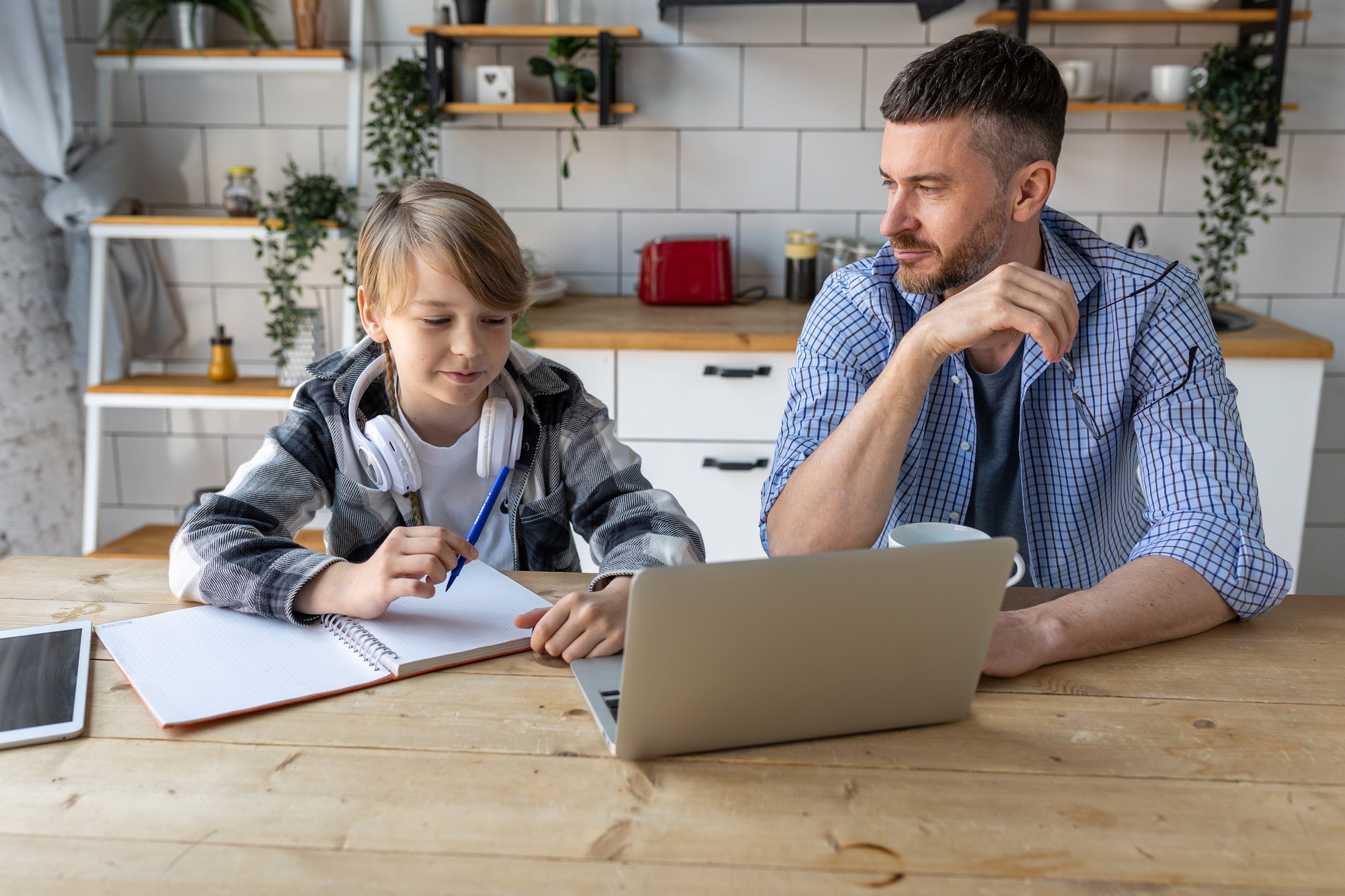 Father helping his teenage son with homework while working from home in the kitchen